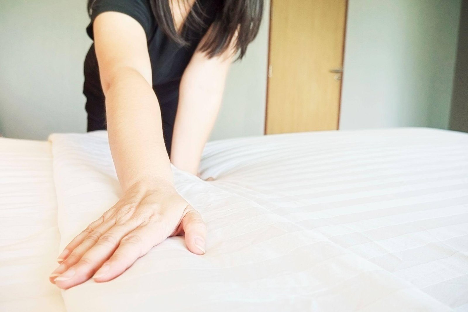 Mulher arrumando o lençol da cama.