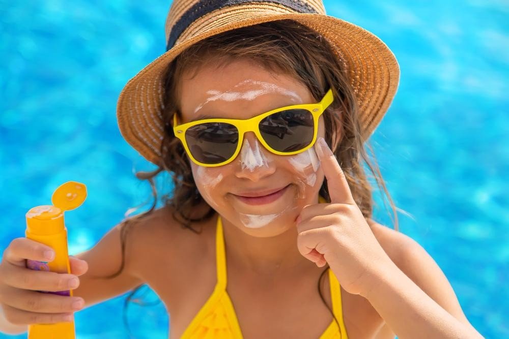 Criança na piscina passando filtro solar em seu rosto