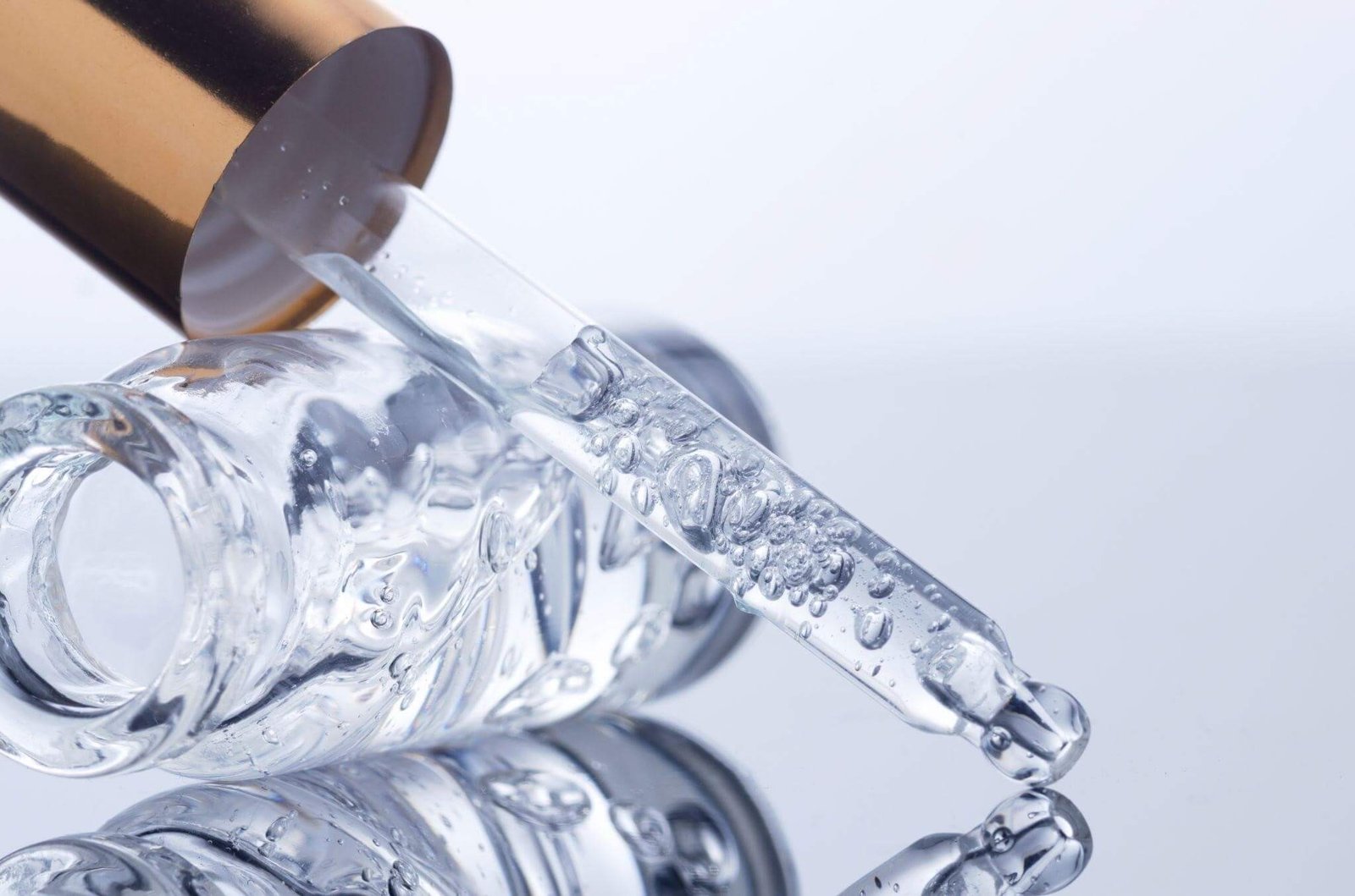 Close-up detalhado de um conta-gotas de vidro com textura de gel transparente sobre um frasco. As bolhas no líquido sugerem a densidade de produtos estéticos, como séruns de colágeno e ácido hialurônico para tratamentos dermatológicos.